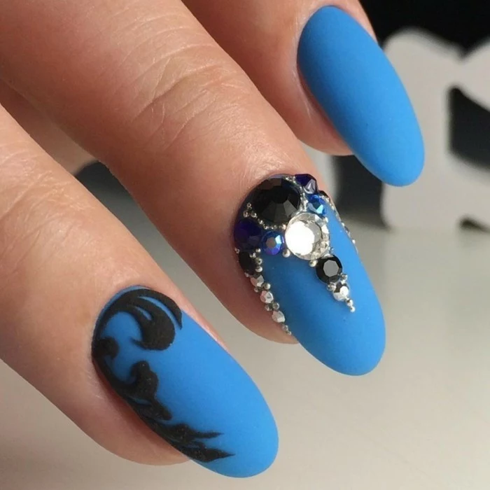 vivid blue matte nail polish, on three nails, one decorated with black sticker, one with black and white rhinestones