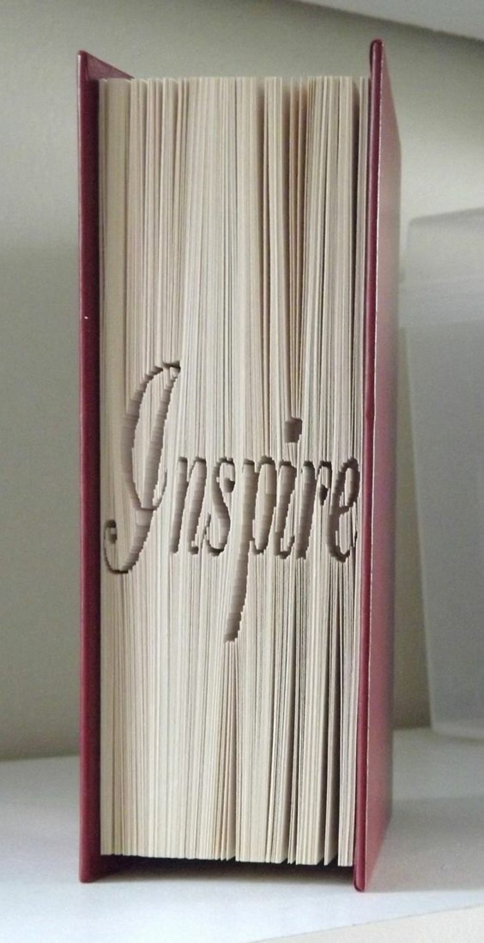 folded book art, closed book with hard purple covers, folded pages spelling the word inspire, in fancy writing