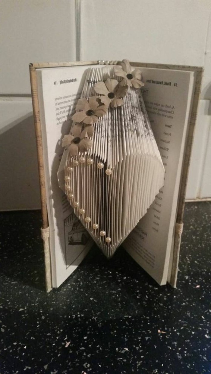 folded book art, heart shape made from folded pages, decorated with white pearly beads, and paper flowers, inside an opened book, with hard covers