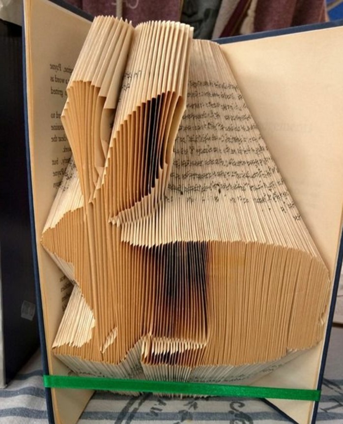 folded book art patterns, rabbit shape made from folded yellowy pages, inside an open book with dark blue hard covers, tied with a green ribbon