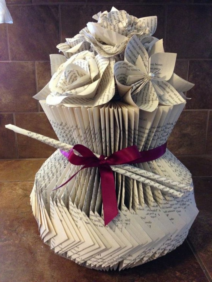 folded book patterns, a vase with flowers, all made from cut and folded book pages, decorated with a purple ribbon