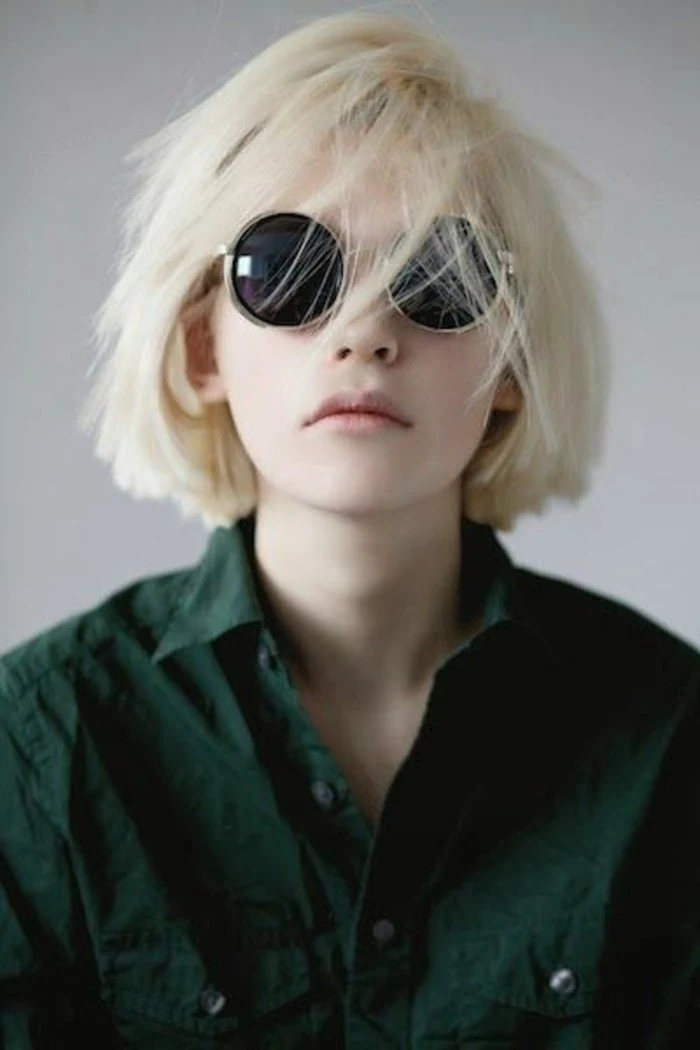 cute hairstyles, young woman with messy platinum blond bob, several strands on her face, wearing black round sunglasses and dark green shirt