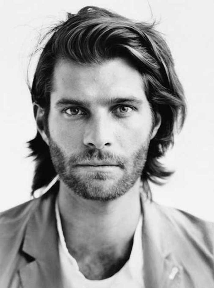 man with wavy layered hair, bangs swept to one side, very short mustache and beard, wearing blazer and white t-shirt