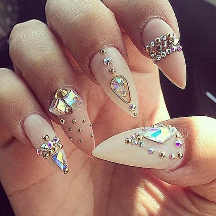 close up of five sharp nails, painted in nude colors in different shades, and decorated with differently shaped and sized rhinestones