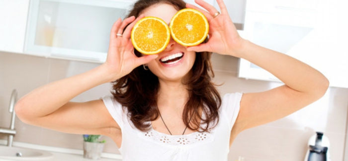 hazel eye color, laughing woman with wavy brown hair and white teeth, holding two orange slices in front of her eyes