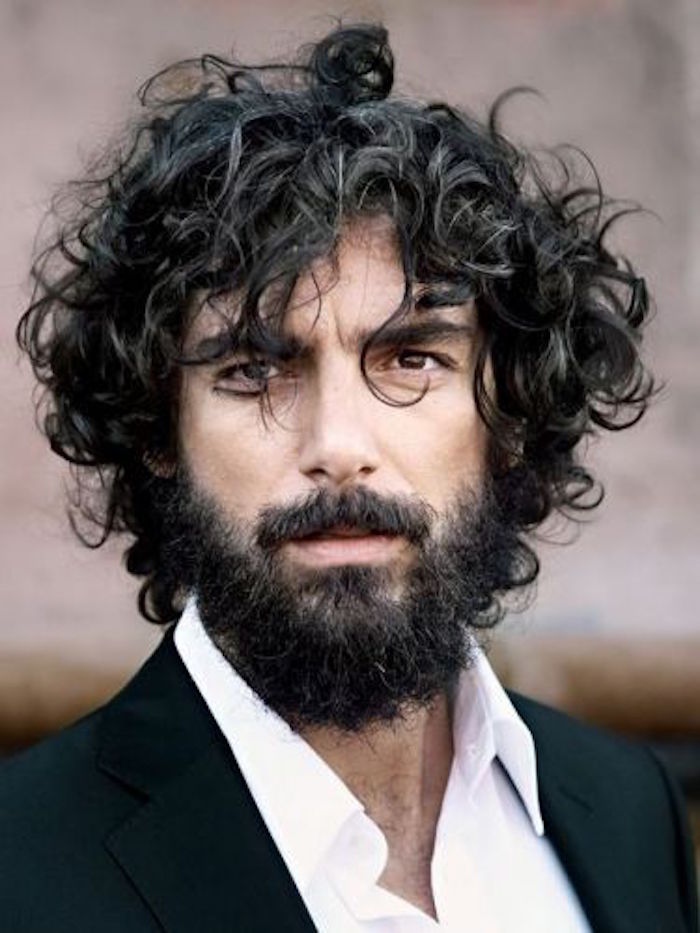close up of man with messy curly black hair, curly black beard and mustache, wearing white shirt and black blazer