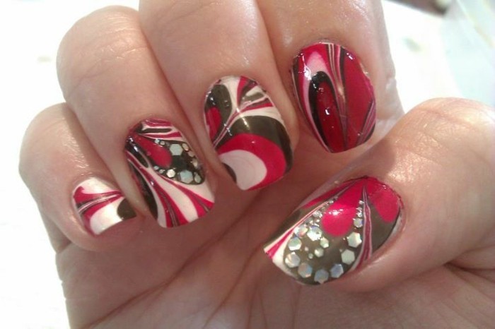 close up of hand with marble-effect nail polish, red brown and white, decorated with tiny rhinestones