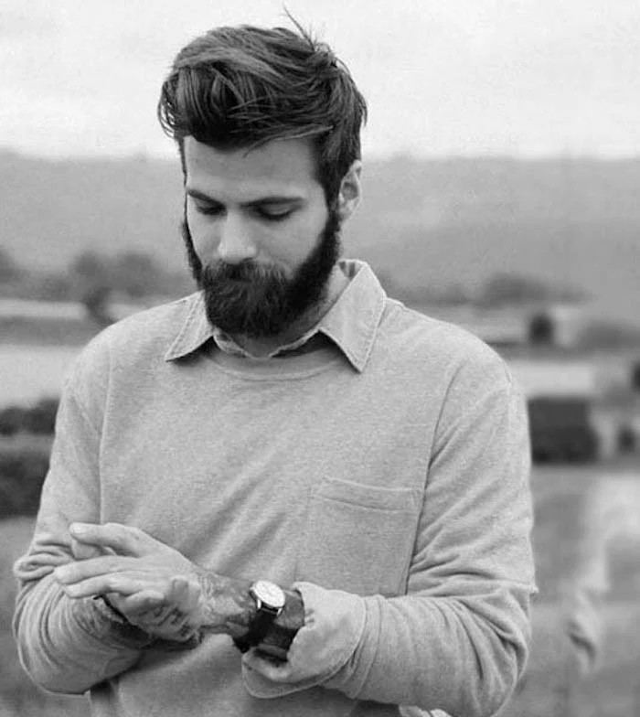 medium length hair, bearded man looking down, gelled-up messy hair in pompadour style, arm tattoos and watch