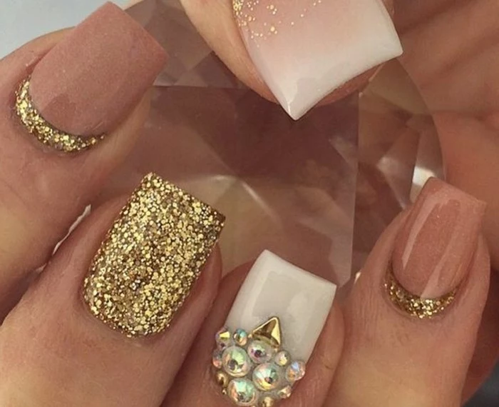 extreme close up of nails painted in white, dark nude and glittering gold, white nail decorated with pearl-shaped rhinestones