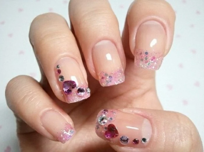 nails with rhinestones, close up of hand with square nails, pale shiny nail polish, pink glitter with round and heart-shaped stones
