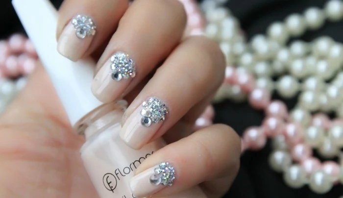 nails with rhinestones, hand holding a bottle of nude colored nail polish, nails painted in same color with rhinestone decorations