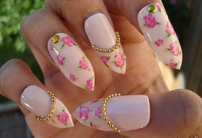 bling bling nails, close up of long, sharp fake nails, painted with pale pastel pink nail polish, and decorated with rose stickers and gold details