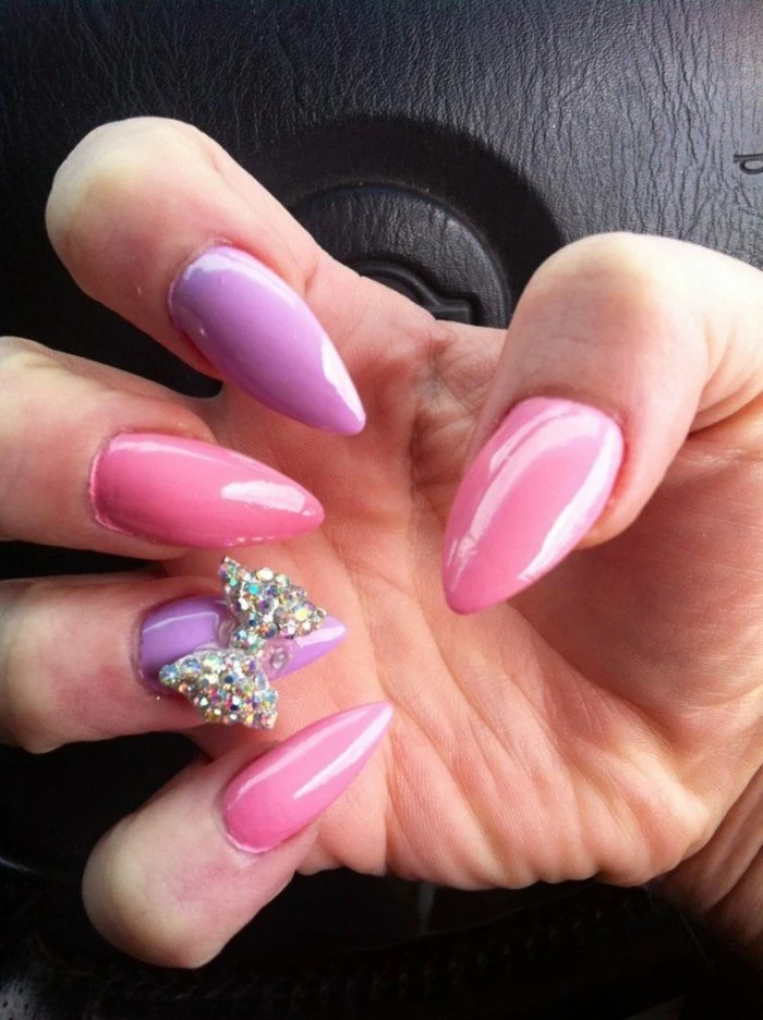 bling bling nails, close up of hand with sharp, pastel pink and pale lilac nails, one of which has a rhinestone bow decoration