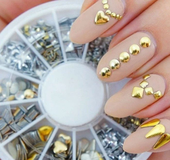 bling bling nails, four long round nails with nude nail polish, decorated with golden 3D stickers, box with more stickers in the background