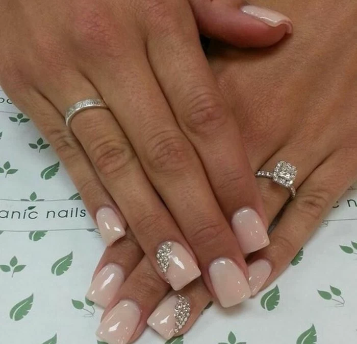 nude nails with rhinestones, square nails painted in nude polish, two decorated with rhinestones