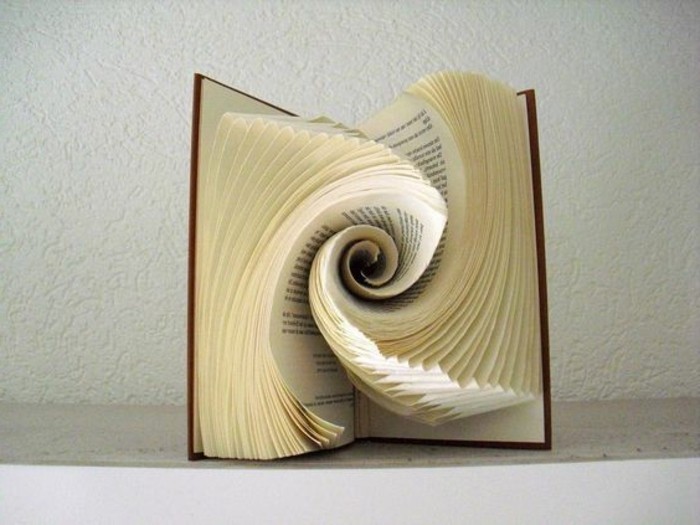 opened book with brown hard covers, containing paper art, made from folded pages, shaped into a swirling round pattern