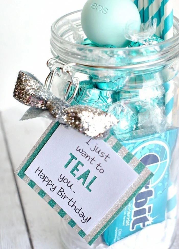 close up of open clear jar, filled with sweets and gum in teal wrappers, birthday card attached to jar with glittering silver bow