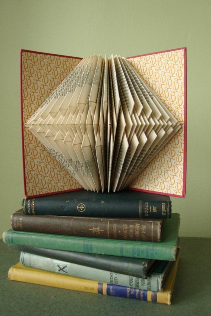 vintage book with red hard covers, placed on a pile of vintage books, and opened to reveal geometrical pattern, created from many folded pages