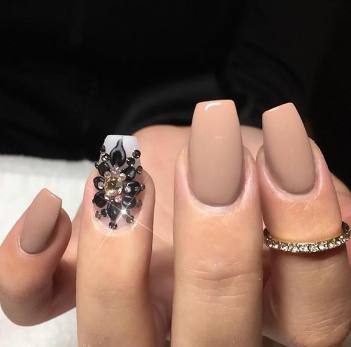 nails with rhinestones, hand with square nails, painted with nude polish, one finger has white and black decoration with rhinestones