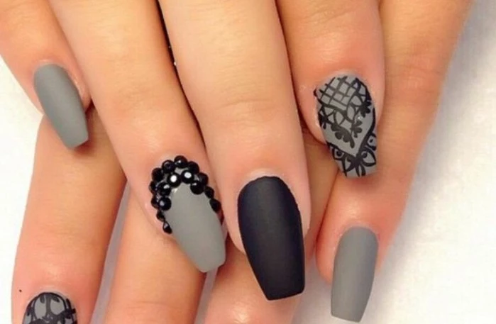 rhinestone nail designs, close up on fingers with grey and black matte nails, decorated with black drawings and stones 