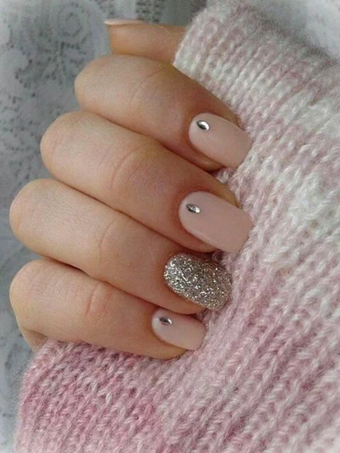 rhinestone nail designs, close up of hand holding pink woolen fabric, four nails painted in pale pink with rhinestone details, one decorated with silver glitter