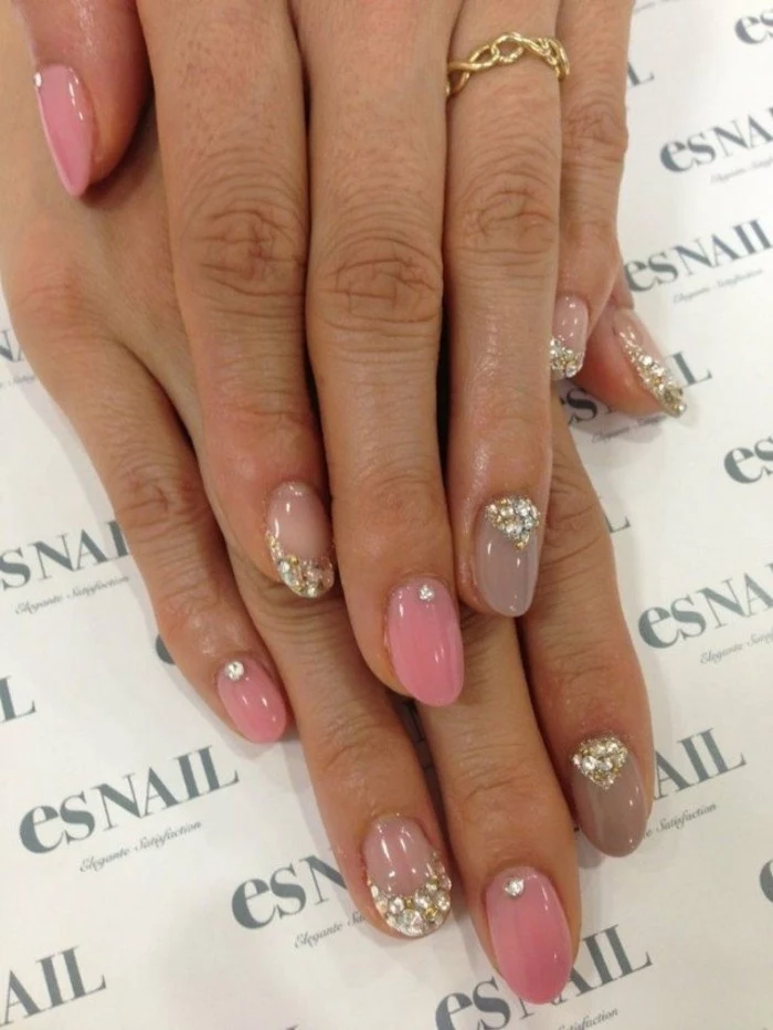rhinestone nail art, two hands with fingernails painted in different shades of pastel pink, decorated with glitter and rhinestones