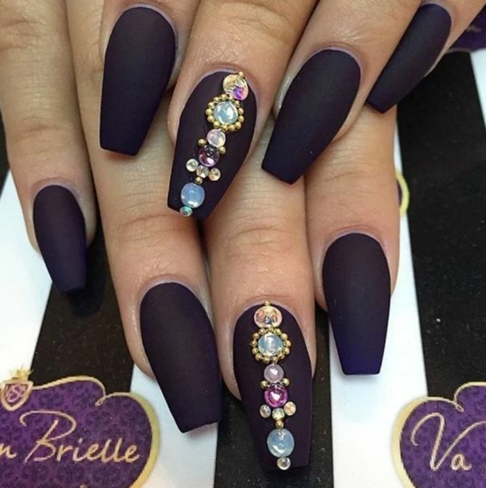 nail designs with rhinestones and glitter, two hands with dark purple square nails, two decorated with multicolored rhinestones