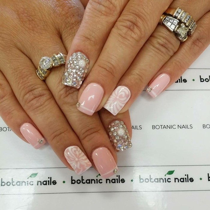 rhinestone nail designs, two hands with rings, wearing pink and white nail design, index fingers' nails covered in rhinestones