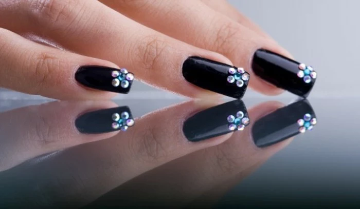 rhinestone nail designs, three fingers resting on a reflective surface, with black nails decorated with rhinestone flowers