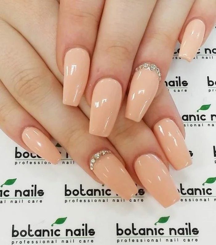 nude nails with rhinestones, two hands with nails painted in pale nude polish, two decorated with several rhinestones