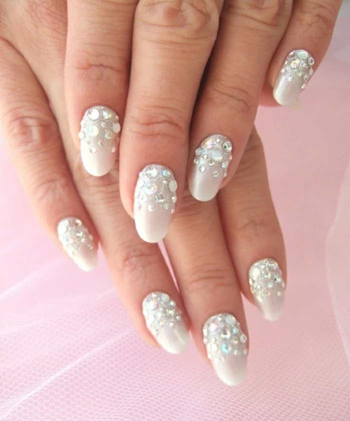 hands with round nails, painted in creamy white nail polish, decorated with round, silvery white rhinestones