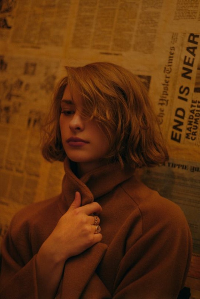 haircuts for women, woman with brown, side-parted wavy bob, wearing a brown woolen coat, and holding its lapel with one hand