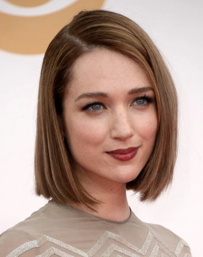haircuts for women, smiling woman with straight, side-parted dark blonde bob, with red lipstick and a nude-colored top 