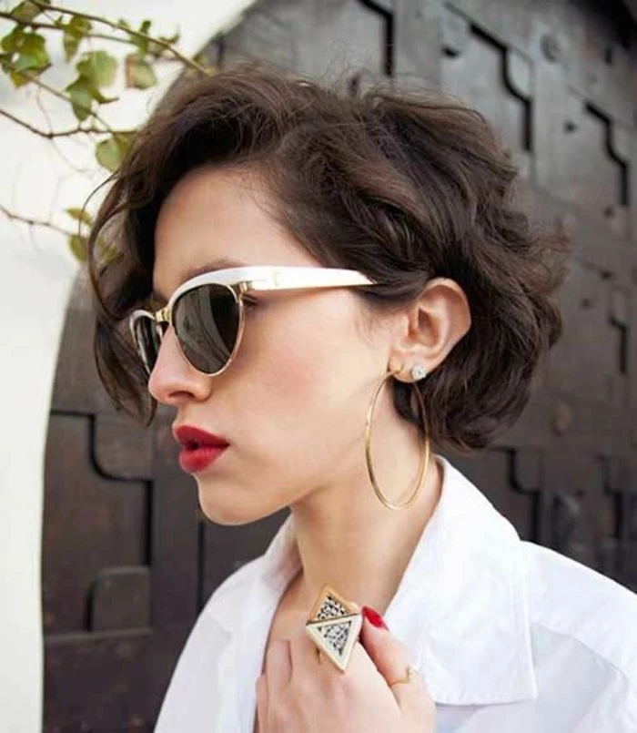 haircuts for women, woman with dark brown, side-parted curly hair, wearing sunglasses with white frames and bright red lipstick