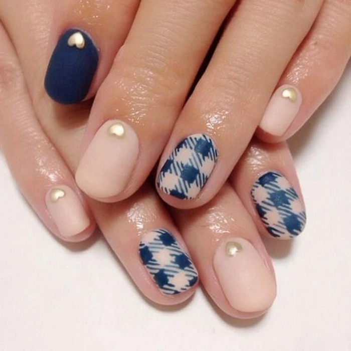 two hands with short nails, painted in pale pink and dark blue matte polish, with tiny gold hearts and chequered detail