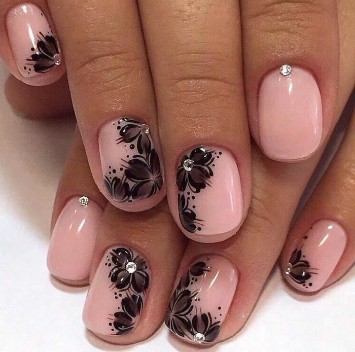 close up of pale pink nails, decorated with black painted flowers, and tiny rhinestones
