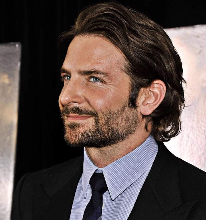 medium length hair, smiling man with stubble beard, dressed in suit and tie, wavy hair slicked back and tucked behind ear