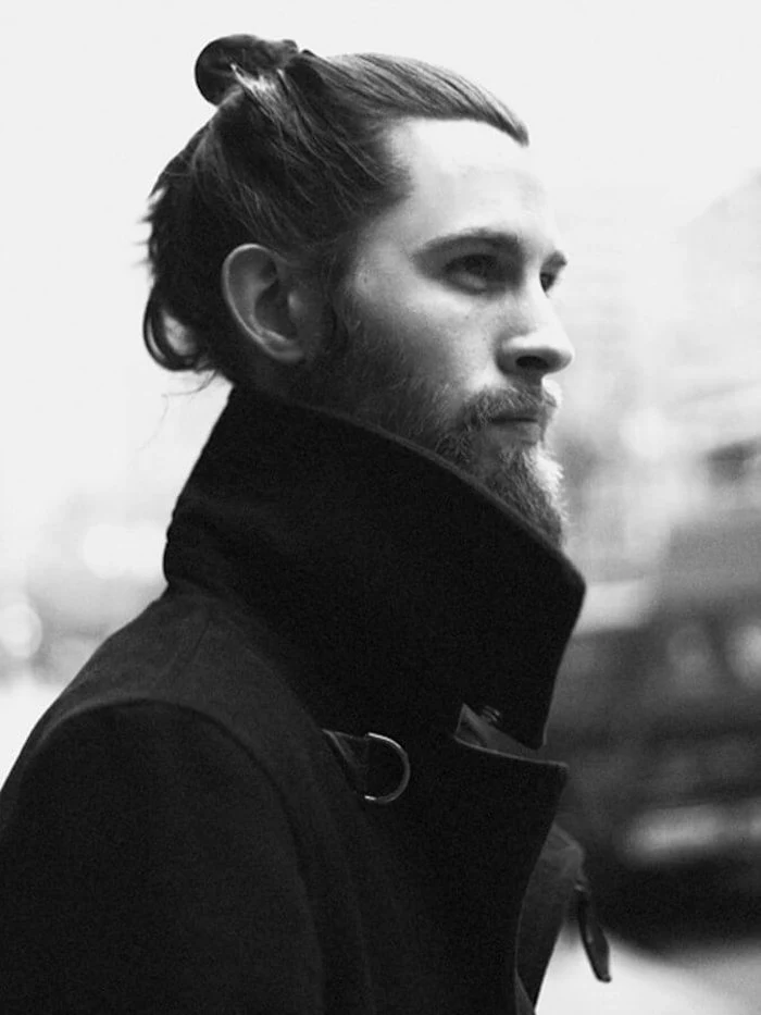 mid length hair, bearded man with man bun, wearing black coat with big collar, looking to the side