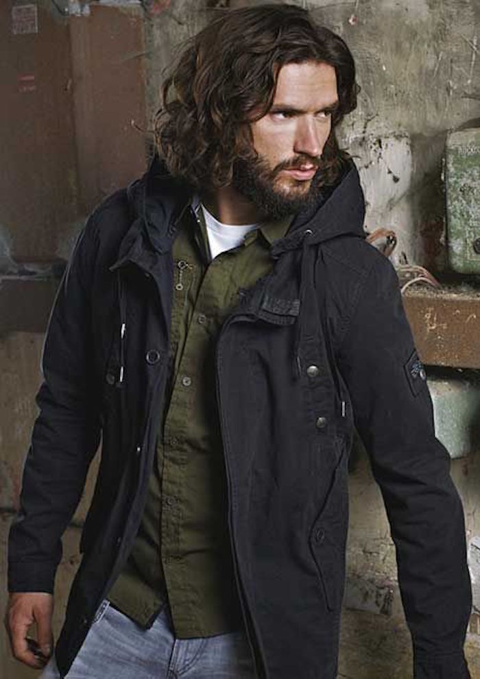 shoulder length hairstyles, man with curly brown hair, with mustache and beard, wearing dark parka over green shirt