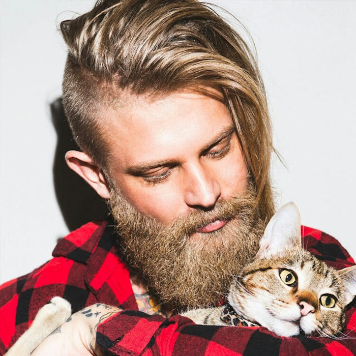 hairstyles for medium length hair, blonde man with undercut, hair swept over to one side, big beard and mustache, plaid shirt and cat