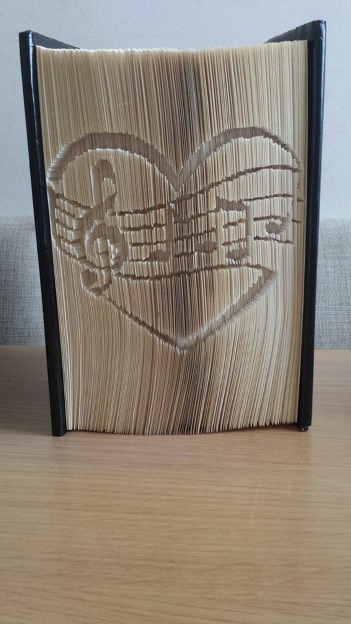 a heart shape with several musical notes, carved into the pages of a thick closed book, with shiny black hard covers