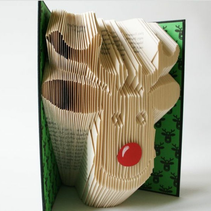 smiling reindeer head, created from folded pages, with red nose made, from round piece of paper, inside an open book, with black and green hard covers