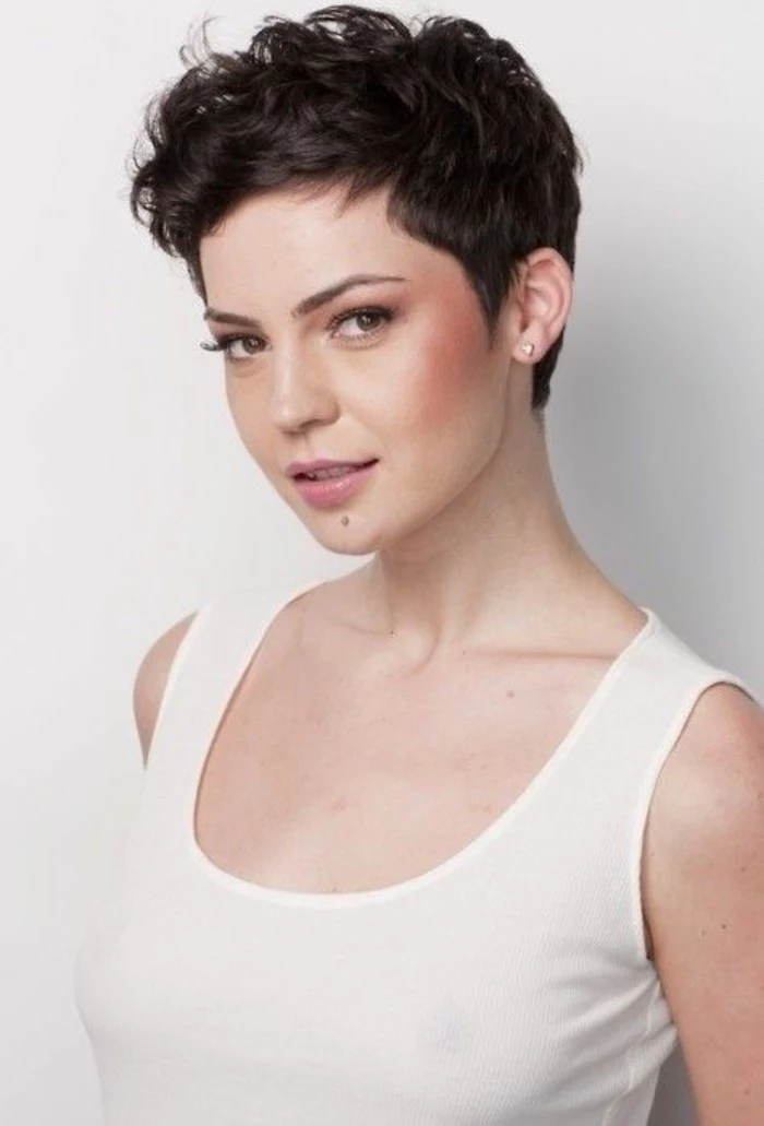 woman with very short and curly, dark brown masculine haircut, wearing white tanktop
