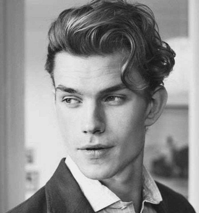 smiling young man with curly hair, swept to one side with a curly strand falling on his forehead