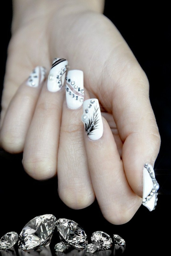close up of hand with long square nails, painted in white nail polish, decorated with black drawings and rhinestones