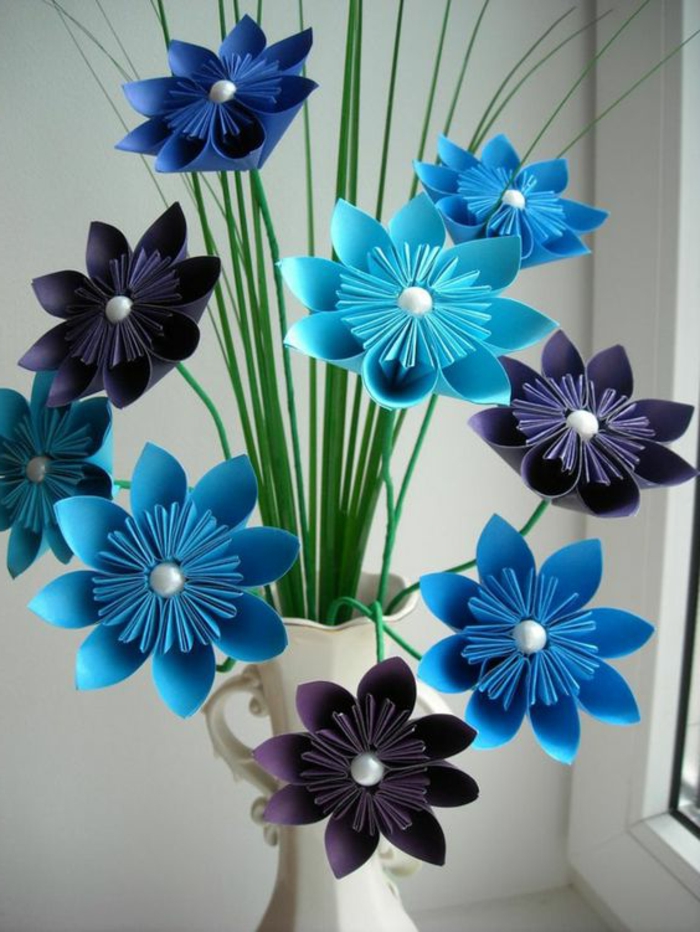 summer diys, several paper origami flowers in violet and blue, decorated with white pearl pins, with sharp green paper leaves, placed in white ornate vase