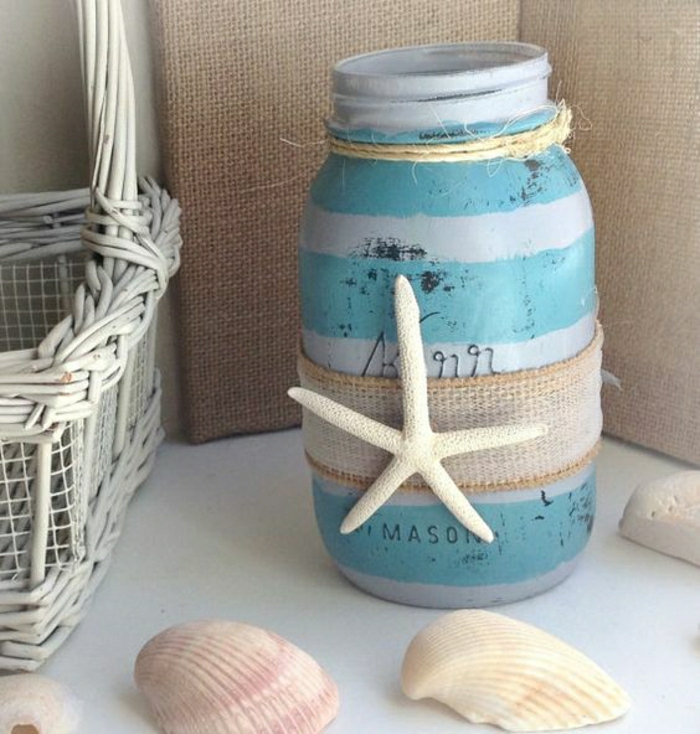 summer crafts for adults, open mason jar, painted in turquoise and light blue stripes, decorated with burlap and a single dried starfish, white whicker basket, and several seashells nearby
