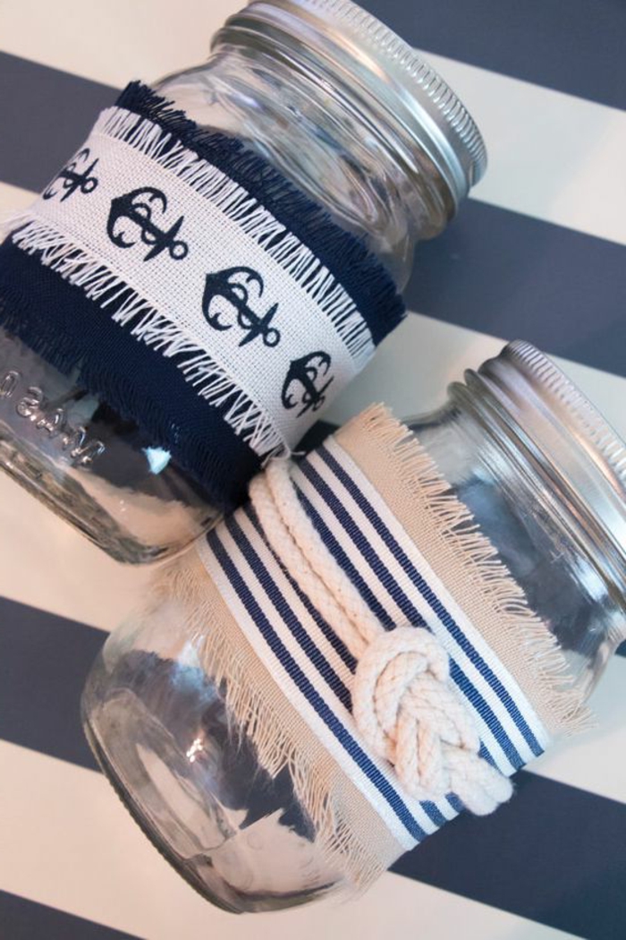 summer crafts, two mason jars, with screw lids, decorated with white and navy blue fabric, with nautical patterns, and rope tied in sailor's knot