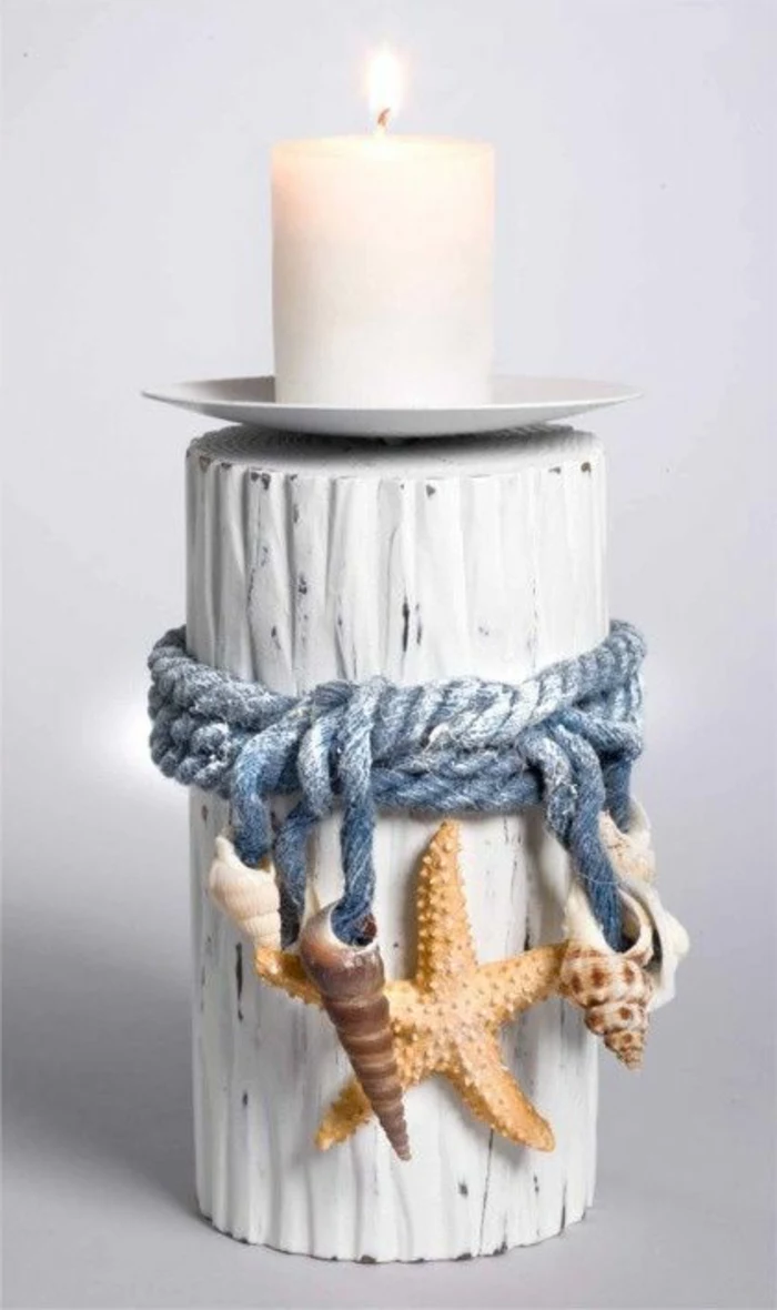 summer crafts for adults, white lit candle, on a small white saucer, placed on a wooden holder, painted white and decorated with seashells and starfish, tied with a faded blue rope