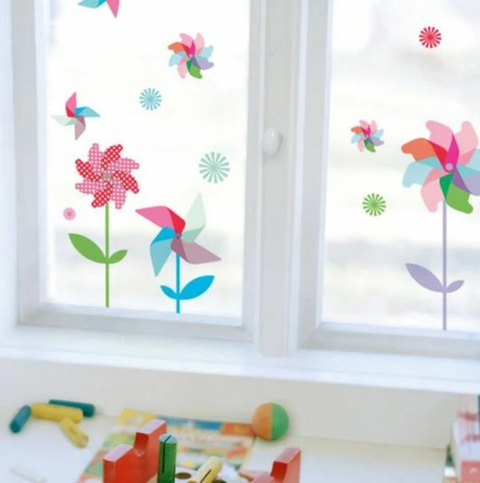 summer craft ideas, window with white panes, decorated with multicolored 2D flower stickers, shaped like wind spinners, colorful kid's toys strewn about